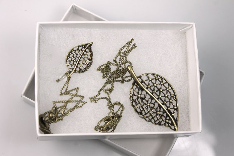 May include: A delicate gold necklace with two leaf-shaped pendants. The leaves are made of intricate metalwork and have a filigree design.