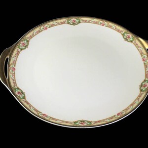 May include: A white oval serving dish with gold trim and floral designs. The dish has two handles on the sides.
