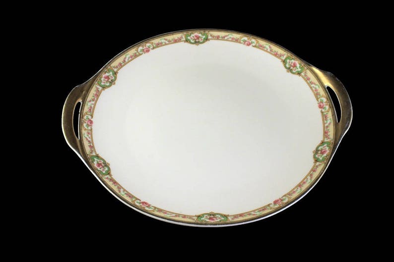 May include: A white oval serving dish with gold trim and floral designs. The dish has two handles on the sides.