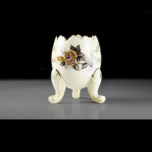 May include: A white ceramic egg-shaped planter with three legs and a floral design featuring yellow roses and brown leaves.