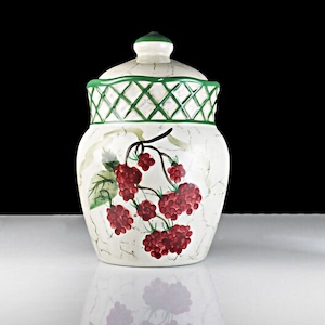 Puede incluir: Jarrón de cerámica blanca con tapa verde y diseño de celosía verde. El jarrón está decorado con un diseño pintado de bayas rojas en una vid.
