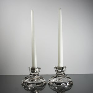 Puede incluir: Dos candelabros de cristal transparente con velas blancas. Los candelabros tienen un dise&ntilde;o festoneado.