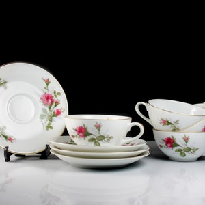 Peut inclure: Un ensemble de quatre tasses &agrave; th&eacute; et soucoupes blanches avec un motif floral repr&eacute;sentant des roses roses et des feuilles vertes. Les tasses et les soucoupes sont empil&eacute;es les unes sur les autres.