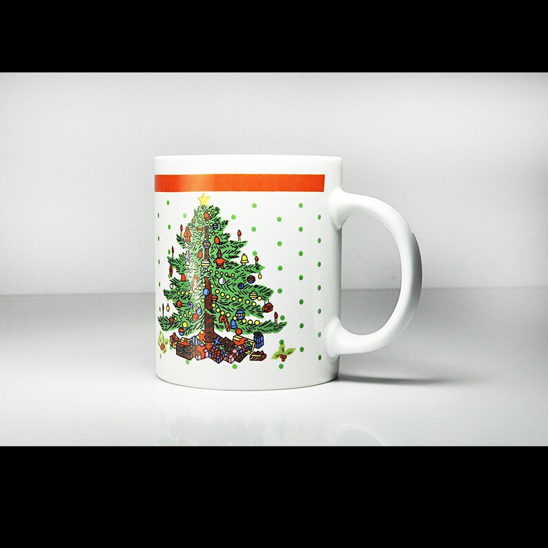 May include: White ceramic mug featuring a green Christmas tree with red and white polka dots. The tree is adorned with baubles and presents.