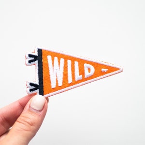 May include: Orange felt pennant with white stitching and the word "WILD" in white letters. The pennant has black felt tabs on the top.
