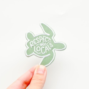 May include: A green embroidered patch shaped like a sea turtle with the text "Respect the Locals" in white.