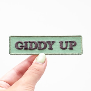 May include: A green fabric patch with brown embroidered text that reads "Giddy Up".