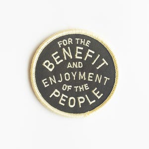 May include: A black and white embroidered patch with a yellow border. The text on the patch reads "For the Benefit and Enjoyment of the People".