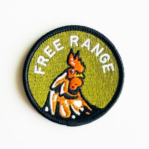 May include: A round, green embroidered patch with a black border. The patch features a white rooster with a red comb and wattle, and the text "FREE RANGE" in white.