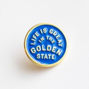 May include: A blue enamel pin with a gold outline. The pin says "Life is great in the Golden State".