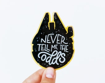 May include: A black and yellow sticker with a silhouette of the Millennium Falcon spaceship from Star Wars. The sticker has the text "Never tell me the odds" written in white.