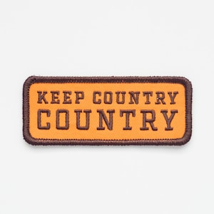 May include: Orange fabric patch with brown stitching and the text "Keep Country Country" in brown lettering.