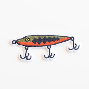 May include: An embroidered fishing lure patch in green, black and orange with three hooks.