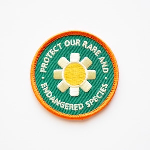 May include: Green and orange embroidered patch with a white flower and yellow center. The text reads "Protect Our Rare and Endangered Species."