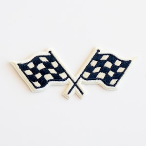 May include: Two white checkered racing flags crossed over each other. The flags are black and white and have a white background.