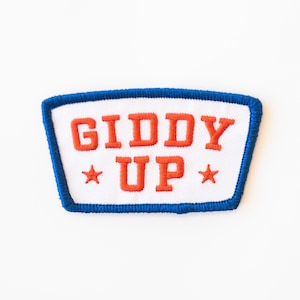 May include: White embroidered patch with blue edging. The patch says "Giddy Up" in red lettering with a star on either side of the text.