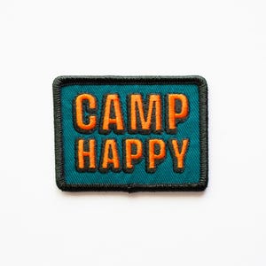 May include: A teal blue embroidered patch with black stitching around the edges. The patch says "CAMP HAPPY" in orange letters.