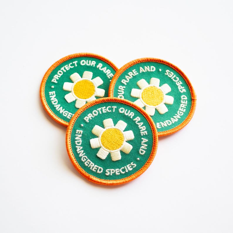 May include: Three green and orange embroidered patches with a white daisy and the text "Protect our rare and endangered species".