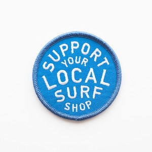 May include: Blue round embroidered patch with white text that reads "Support Your Local Surf Shop".