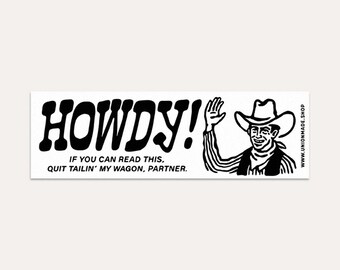 Op de afbeelding: Een rechthoekige witte sticker met zwarte tekst en een cartoon cowboy illustratie. De tekst luidt "HOWDY!" boven de zin "IF YOU CAN READ THIS, QUIT TAILIN' MY WAGON, PARTNER." Een websiteadres staat aan de rechterkant.