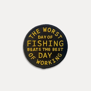 May include: A round, black embroidered patch with yellow text. The text reads "THE WORST DAY OF FISHING BEATS THE BEST DAY OF WORKING". The patch is likely for a jacket or bag.