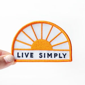May include: Orange and white embroidered patch with a sun design and the text "LIVE SIMPLY".