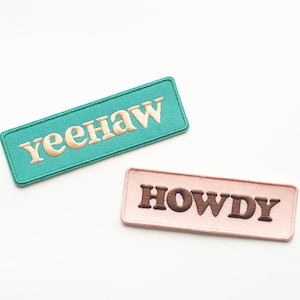 May include: Two embroidered patches, one turquoise with the text "yeehaw" in gold thread, and one pink with the text "HOWDY" in brown thread.