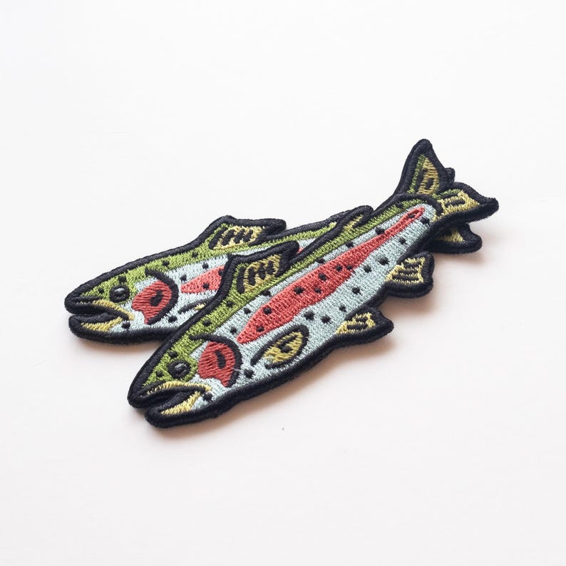 May include: Two embroidered iron-on patches of rainbow trout fish. The patches are green, blue, red, and yellow with black outlines.