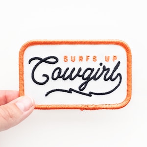 May include: Orange embroidered patch with white fabric and black lettering that reads "Surfs Up Cowgirl".