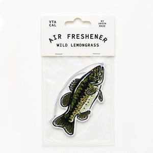 May include: A fish-shaped air freshener in a clear plastic package with a white header card. The text reads VTA CAL, BY UNION MADE, AIR FRESHENER, and WILD LEMONGRASS. The air freshener features a green and black graphic illustration of a fish.