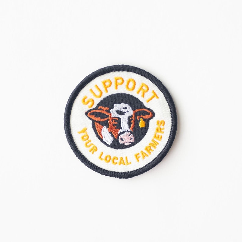May include: A black and white embroidered patch with a cow and the text "Support Your Local Farmers" in orange.