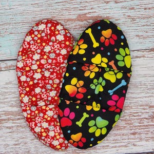 May include: Two heart-shaped fabric pot holders. One is red with white floral print, the other is black with colorful paw prints and bone designs.