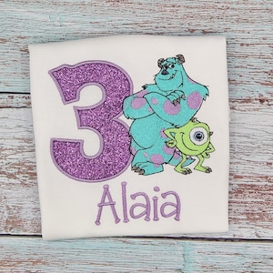 May include: Purple glitter number 3 with embroidered images of Sully and Mike from Monsters Inc. The name Alaia is embroidered below the number.