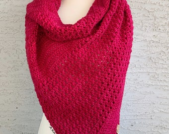 May include: A bright pink crocheted triangular shawl with a textured stitch pattern. The shawl is draped over a white mannequin.