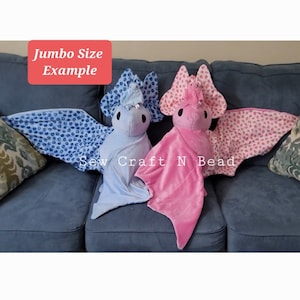 Puede incluir: Dos juguetes de peluche en forma de murci&eacute;lago, uno azul con lunares blancos y otro rosa con lunares blancos, en un sof&aacute; gris. El texto "Jumbo Size Example" est&aacute; en un cuadro rojo encima de los murci&eacute;lagos. El texto "Sew Craft N Bead" est&aacute; debajo de los murci&eacute;lagos.