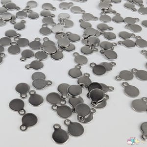 May include: A large quantity of silver metal round disc charms with a small loop at the top. The charms are scattered on a white surface.