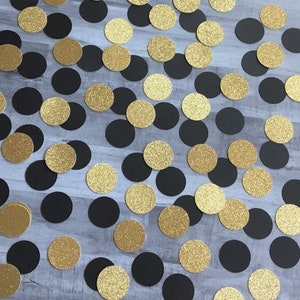 May include: Black and gold glitter confetti circles. The confetti is scattered on a wood surface.