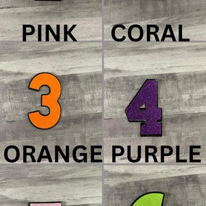 May include: Six colorful numbers, each with a black outline, are displayed against a gray background. The numbers are pink, coral, orange, purple, lilac, and lime green. Each number has a corresponding color name written below it.