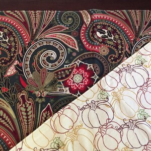 Peut inclure: Deux chemins de table, l'un avec un motif paisley dans des tons de rouge, vert et noir, et l'autre avec un fond blanc et un motif répété de citrouilles brodées dans des tons de brun et de rouge.