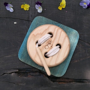 Peut inclure: Un jouet en bois en forme de bouton avec une ficelle blanche passée dans les trous. Le bouton est sur une base en bois bleu et vert.