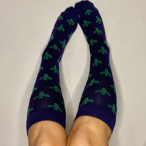 May include: A pair of knee-high socks with a navy blue background and a repeating pattern of green cactus plants.