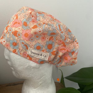 May include: A light pink and blue floral print scrub cap with a white label that says "Sparrow & Co."