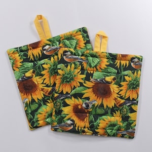 May include: Two quilted pot holders with a sunflower and bird design. The pot holders are black with yellow sunflowers, green leaves, and small yellow birds.