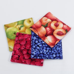 May include: Four fabric coasters with different fruit designs. One coaster features red raspberries, another has blue blueberries, a third has green apples, and the last one has peach slices.