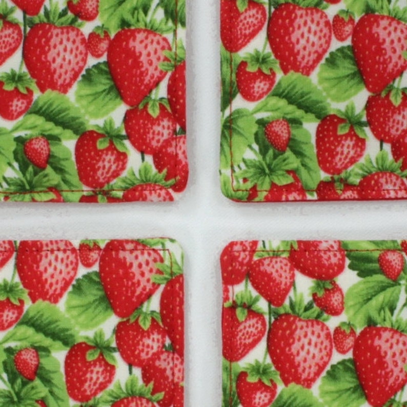 May include: Four square fabric coasters with a white background and a repeating pattern of red strawberries and green leaves.