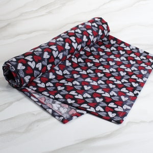 May include: A black and red table runner with a repeating pattern of white and red hearts. The runner is made of fabric and has a soft, textured feel.