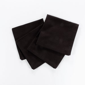 May include: Four black fabric napkins folded neatly on a white surface.