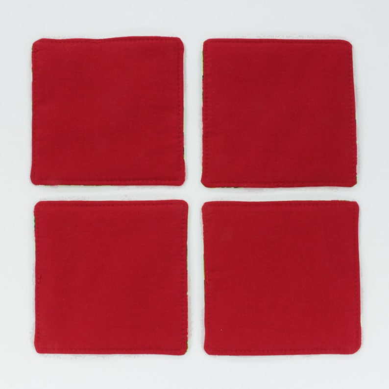 May include: Set of four red and green square coasters. The coasters are made of fabric and have a stitched edge.