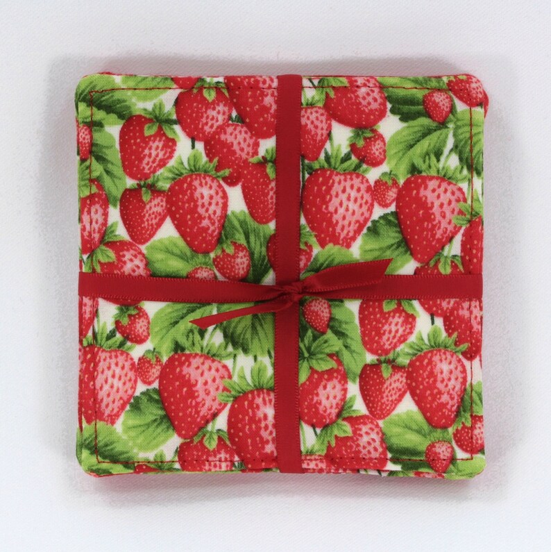 May include: Set of four red and green fabric coasters with a strawberry print. The coasters are tied together with a red ribbon.