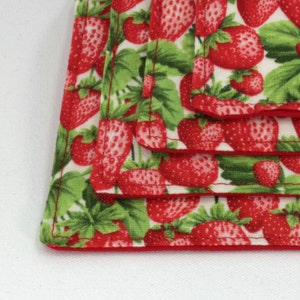 May include: Stack of four red and green fabric squares with a strawberry pattern. The fabric squares are sewn together with a red border.